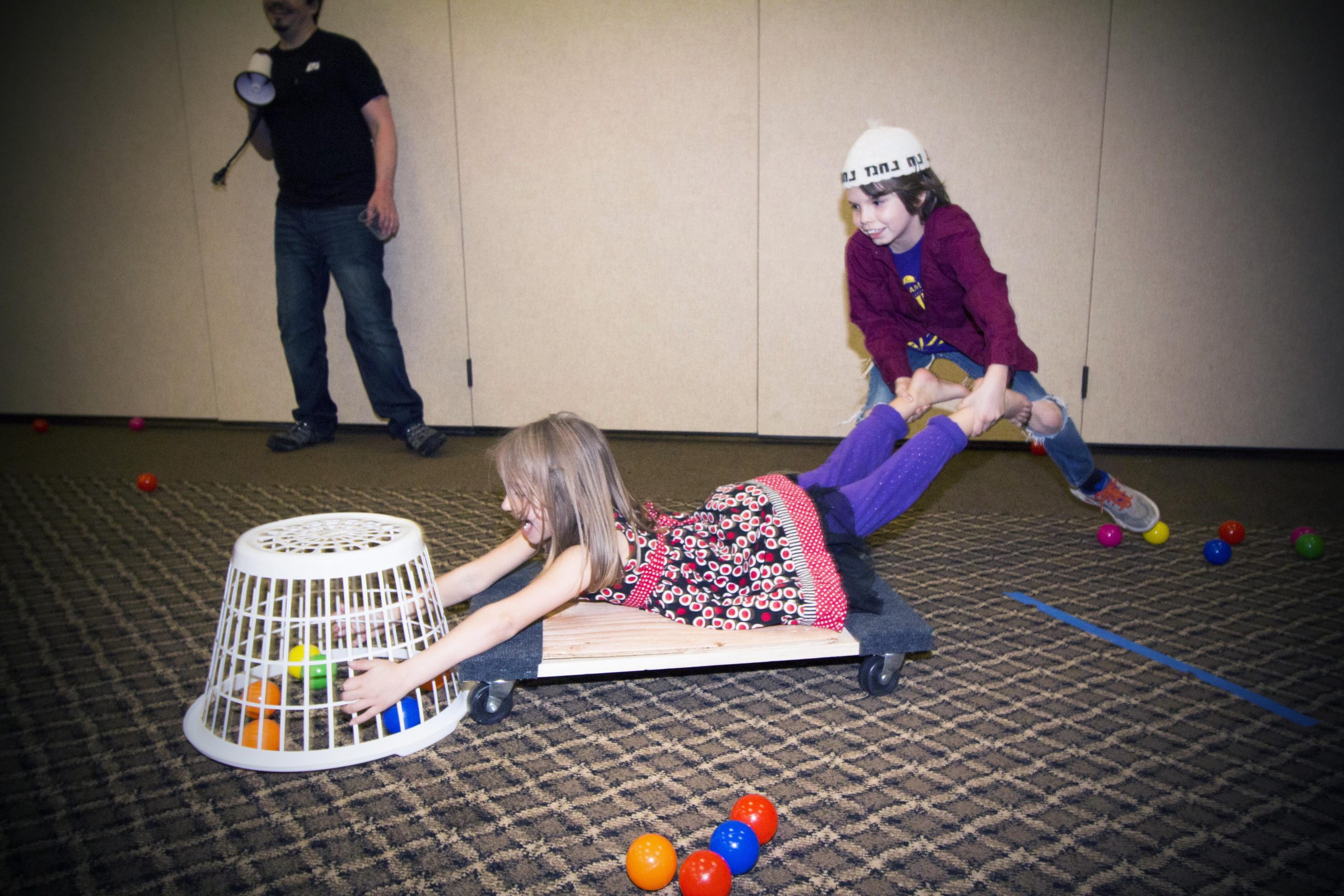 two kids playing a game with one on a dolly catching balls with baskets